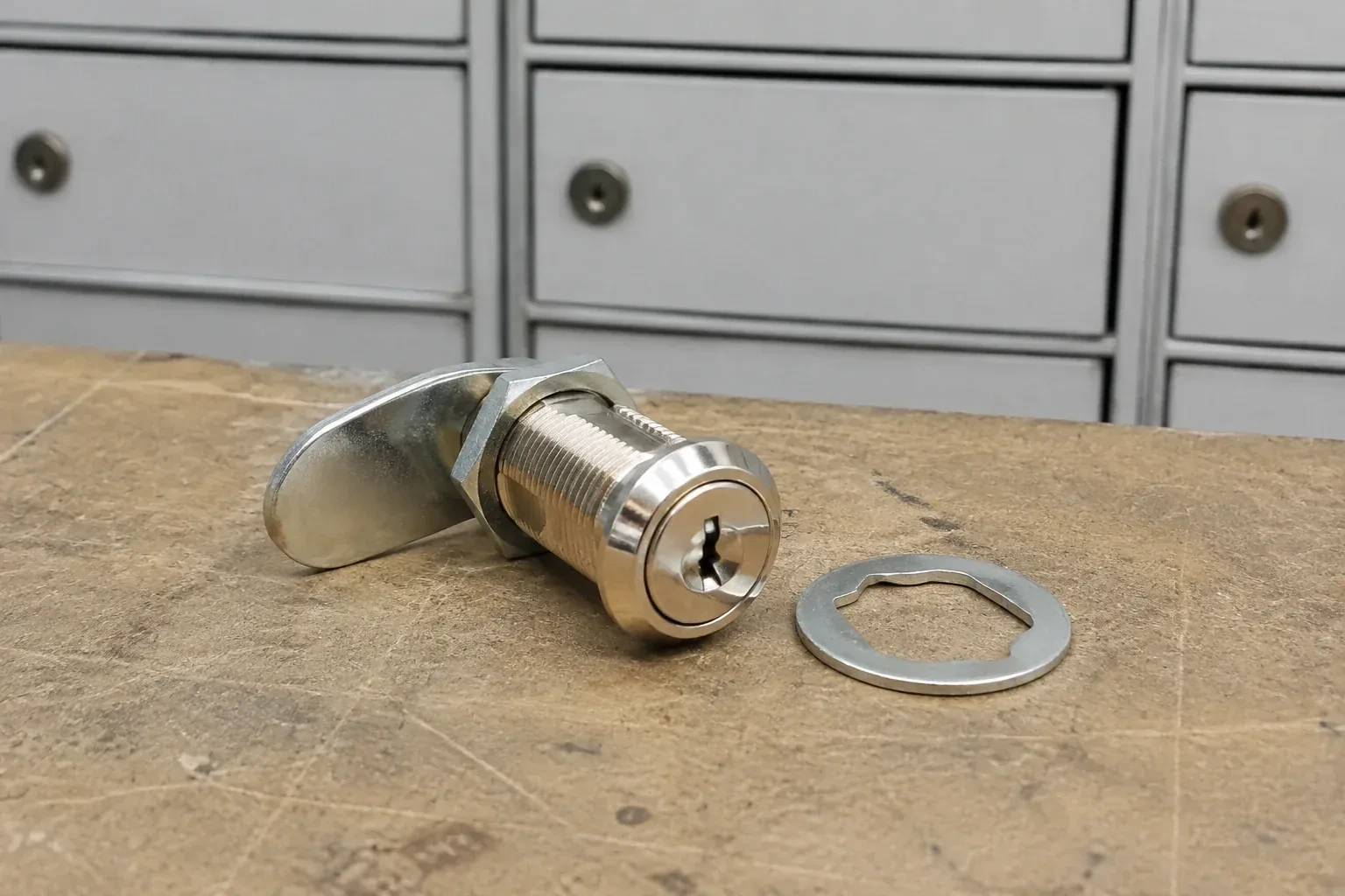 Detached threaded cam lock and mounting washer on a workbench in front of closed mail compartments. — Mailbox Lock Replacement, Georgina